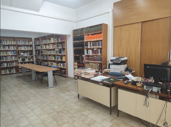Interior da Biblioteca — sala de leitura com estantes e mesa de trabalho