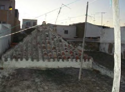 Telhado de tesouro de quatro águas, em telha de canudo, visto de uma açoteia, com fios, antenas e casas vizinhas ao fundo.