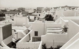 Fotografia antiga a preto e branco de casas brancas de açoteia, com muretes e pequenas chaminés, vistas de um ponto alto.