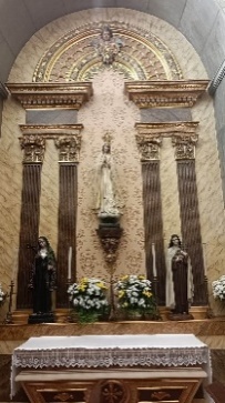 Altar lateral com imagem branca de Nossa Senhora sobre mísula, entre duas imagens de santas de hábito escuro e jarras de flores