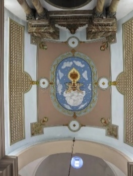 Teto pintado da capela-mor visto de baixo, com medalhão oval azul onde dois anjos sobre nuvens erguem um resplendor dourado