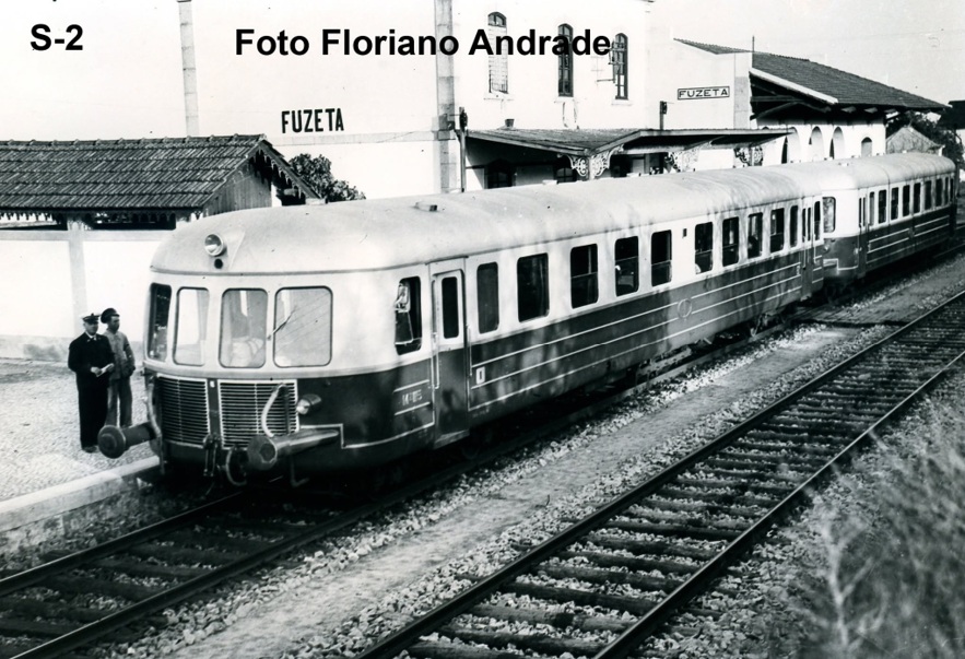 Fotografia antiga a preto e branco: automotora parada na estação de caminho de ferro da Fuzeta, com dois homens fardados na plataforma. Crédito «Foto Floriano Andrade».