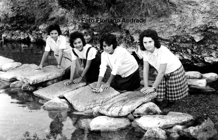 Fotografia antiga a preto e branco: quatro raparigas sorridentes debruçadas sobre as lajes de pedra de um olheiro, com as mãos junto à água. Crédito «Foto Floriano Andrade».