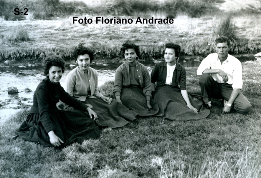 Fotografia antiga a preto e branco: quatro raparigas de saia comprida e um rapaz sentados na relva junto a um curso de água. Crédito «Foto Floriano Andrade».